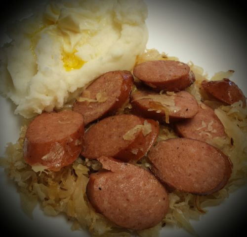 A plate of sliced sausage served on a bed of sauerkraut, accompanied by a scoop of creamy mashed potatoes.
