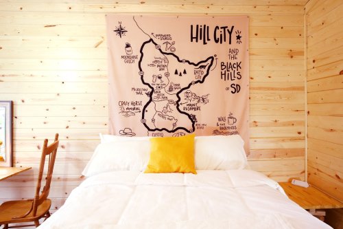 A cozy bedroom featuring a map tapestry of Hill City and the Black Hills of South Dakota above a neatly made bed.