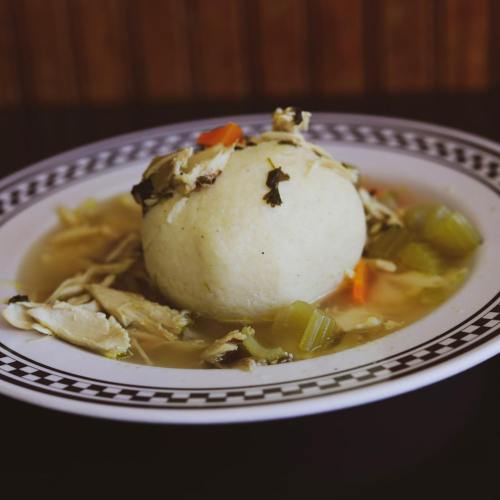 A bowl of chicken soup with a large dumpling, surrounded by vegetables like celery and carrots.