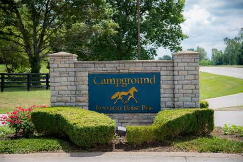 Sign for Campground at Kentucky Horse Park, surrounded by greenery and flowers, with a blue sky in the background.