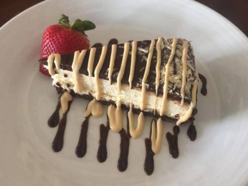 A slice of chocolate dessert topped with drizzled peanut butter and coconut, served with a fresh strawberry.
