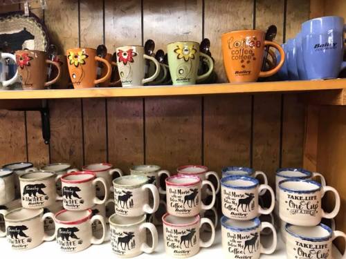 A shelf displaying various colorful coffee mugs with decorative designs and text, arranged neatly.