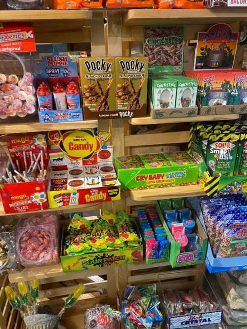 A colorful display of various candies and snacks on wooden shelves, including Pocky, gummies, and lollipops.