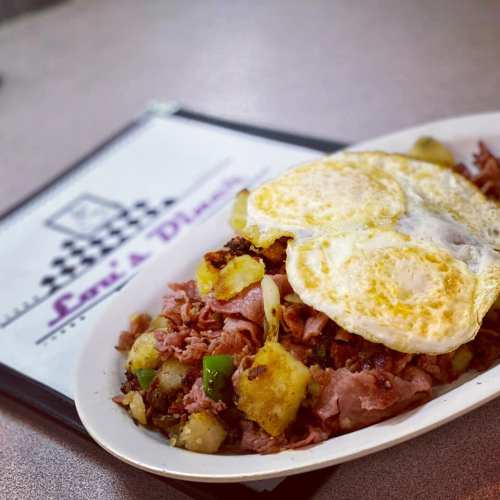 A plate of hash with ham, potatoes, and two sunny-side-up eggs, with a menu in the background.