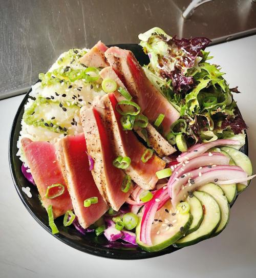 A vibrant bowl of sushi-grade tuna slices on rice, garnished with greens, cucumbers, and sesame seeds.