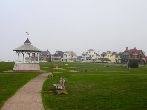A foggy park scene featuring a gazebo, benches, and historic houses in the background.