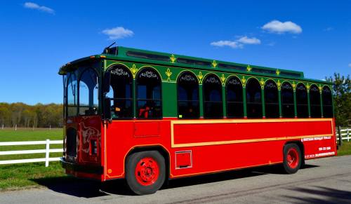 A colorful red and green trolley bus parked beside a white fence under a clear blue sky.