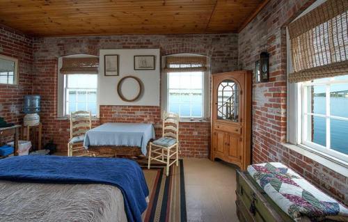 Cozy bedroom with brick walls, a bed, wooden furniture, and windows overlooking a water view.