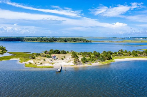 Aerial view of a serene coastal landscape with a small island, dock, and lush greenery under a blue sky.