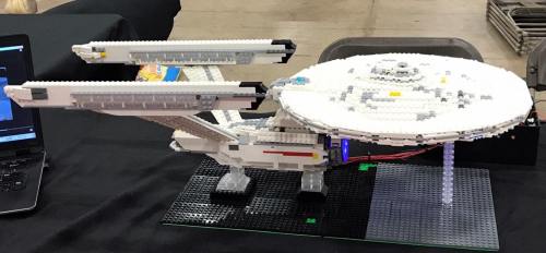 A detailed LEGO model of a starship, displayed on a table with a laptop nearby.