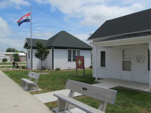 A small park with benches, a flagpole, and colorful signage near white buildings on a sunny day.