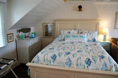 Cozy bedroom with a bed featuring a sea-themed quilt, nightstand, lamp, and decorative coastal accents.