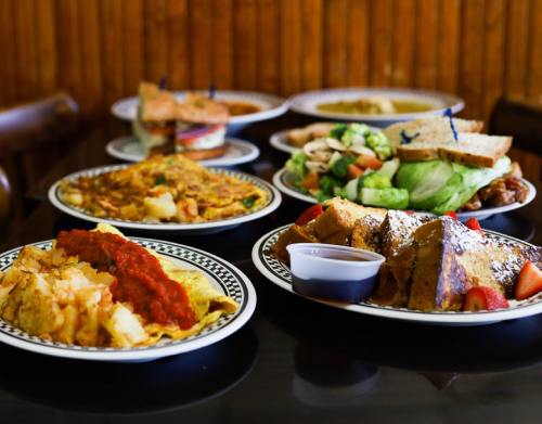 A variety of delicious dishes on plates, including omelets, sandwiches, salads, and French toast, on a table.