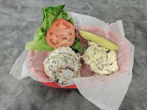 A red basket with two scoops of salad, lettuce, a slice of tomato, and a pickle, all on parchment paper.