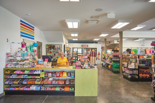A brightly lit convenience store with a colorful candy display and a cashier at the counter. Shelves are stocked with various items.