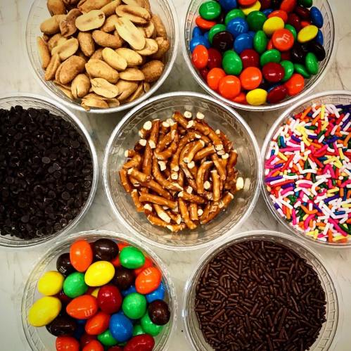 A variety of colorful candies and snacks in clear bowls, including nuts, pretzels, chocolate chips, and sprinkles.