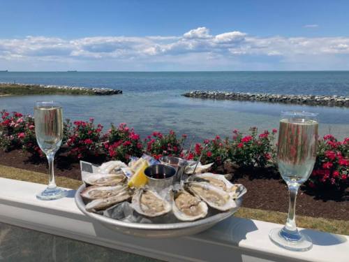 A platter of oysters with lemon and sauce, flanked by two glasses of sparkling wine, overlooking a serene waterfront.