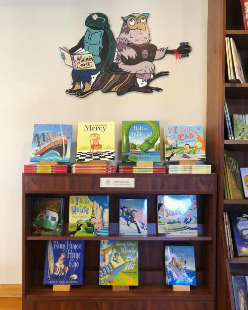 A wooden bookshelf displays colorful children's books, with a cartoon owl and turtle mural above.