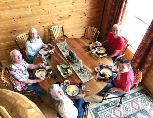 A group of five people enjoying a meal around a wooden table in a cozy, rustic setting.