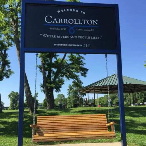 Sign welcoming visitors to Carrollton, KY, with a park setting and a swing in front of a gazebo.