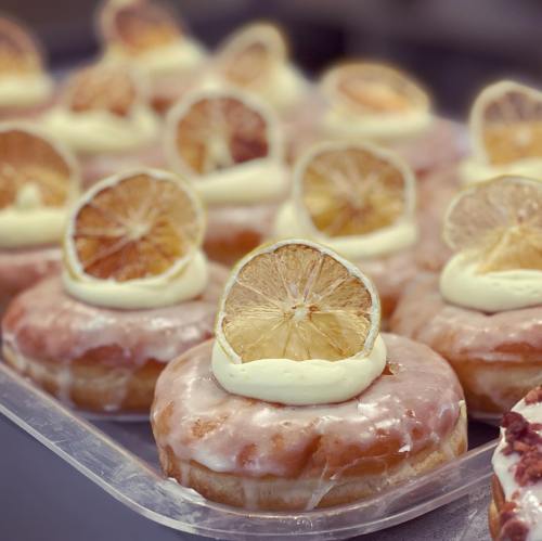 A close-up of glazed donuts topped with cream and dried lemon slices, arranged on a tray.