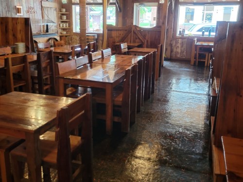 Interior of a rustic restaurant with wooden tables and chairs, featuring a polished floor and warm lighting.