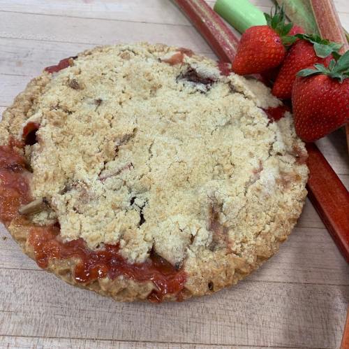 A freshly baked strawberry rhubarb pie with a crumbly topping, accompanied by fresh strawberries and rhubarb stalks.