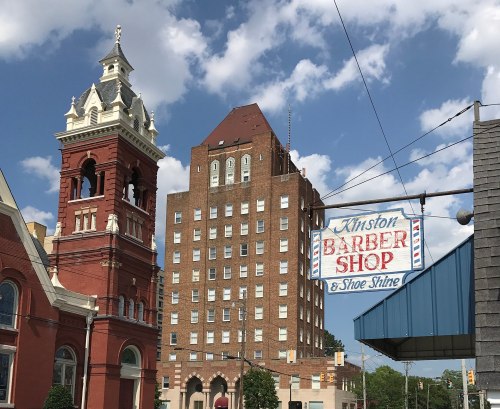 A historic barber shop sign in front of a tall brick building under a partly cloudy sky.