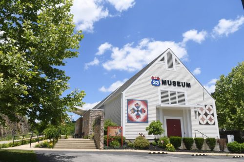 Exterior of a white museum building with a sign reading "Museum," surrounded by greenery and blue skies.