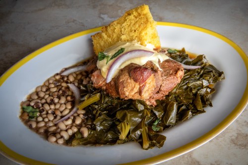 A plate of collard greens, black-eyed peas, and a meat dish topped with sauce and garnished with onions and cornbread.