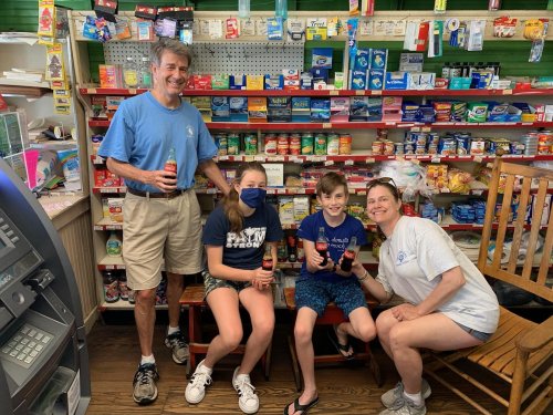 A family poses in a store, holding drinks, with shelves of snacks and products in the background.
