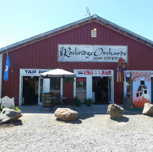 Red barn-style building with a sign reading "Rockridge Orchards and Cidery," featuring outdoor seating and an open sign.