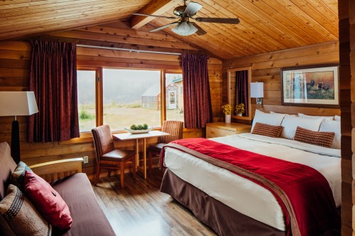 Cozy wooden cabin interior with a king bed, seating area, and large windows overlooking a scenic view.