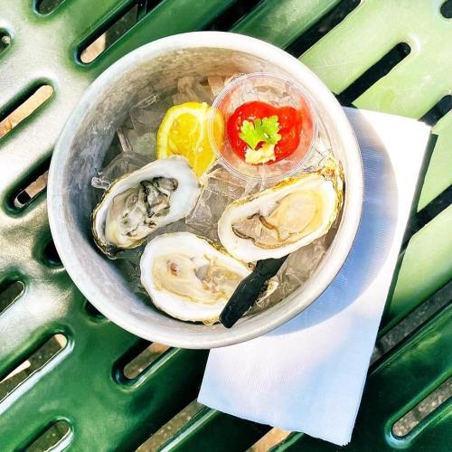A bowl of fresh oysters on ice, accompanied by lemon wedges and a small cup of cocktail sauce, on a green table.