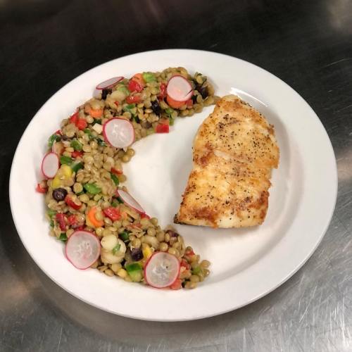 A plate featuring a piece of seasoned fish alongside a colorful grain salad with vegetables and radishes.