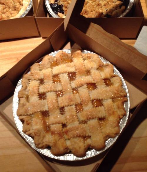 A freshly baked pie with a lattice crust, sitting in a cardboard box on a wooden surface.