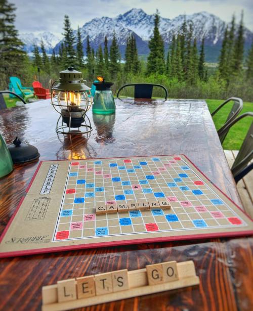 A Scrabble board on a wooden table outdoors, with mountains in the background and the words "LET'S GO" spelled out.