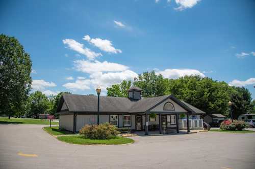 A small, modern building with a cupola, surrounded by greenery and blue skies, set in a park-like area.