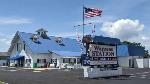 A blue-roofed family restaurant with an American flag and colorful flags outside, set against a clear sky.