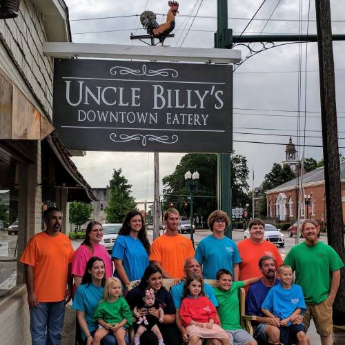 A diverse group of people in colorful shirts poses in front of Uncle Billy's Downtown Eatery sign.