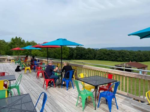 Outdoor seating area with colorful chairs and umbrellas, overlooking a green landscape and distant hills.