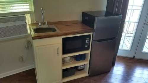 A small kitchen area featuring a sink, microwave, and refrigerator with wooden countertops and shelves.