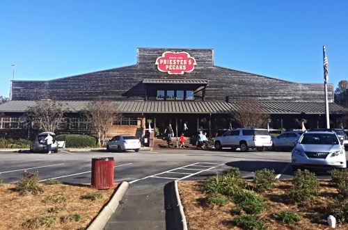 Exterior of Priester's Pecans store with wooden facade, parking lot, and people entering on a sunny day.