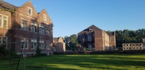 Abandoned brick buildings surrounded by green grass under a clear blue sky.