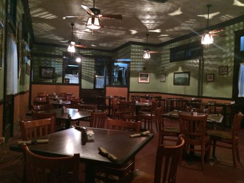 Cozy restaurant interior with wooden tables and chairs, soft lighting, and patterned shadows on the walls.