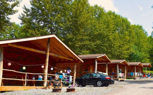 A row of rustic cabins surrounded by trees, with outdoor seating and parked cars in a serene setting.