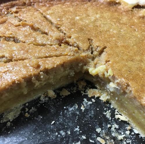 A close-up of a golden-brown pie with a slice removed, revealing a soft, textured filling and a crumbly crust.