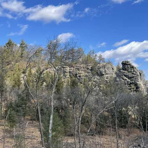 A rocky hillside with sparse trees under a blue sky with scattered clouds.