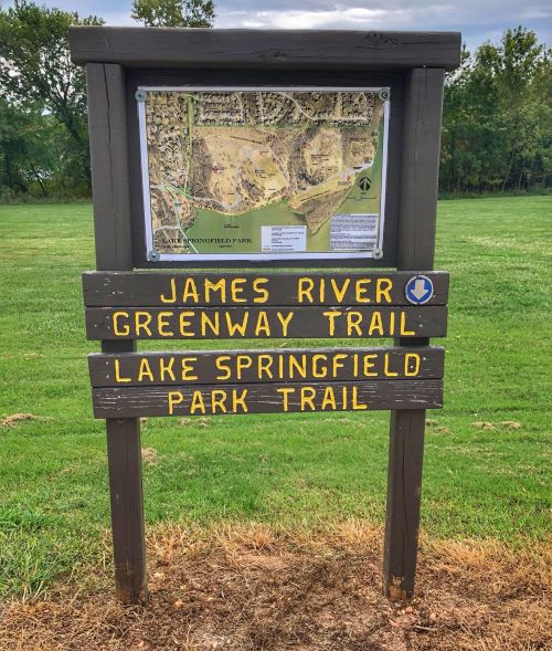 Signpost displaying trails: James River Greenway Trail and Lake Springfield Park Trail, with a map in the background.