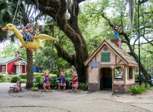 Colorful children's play area featuring a whimsical house and playful animal sculptures under lush trees.